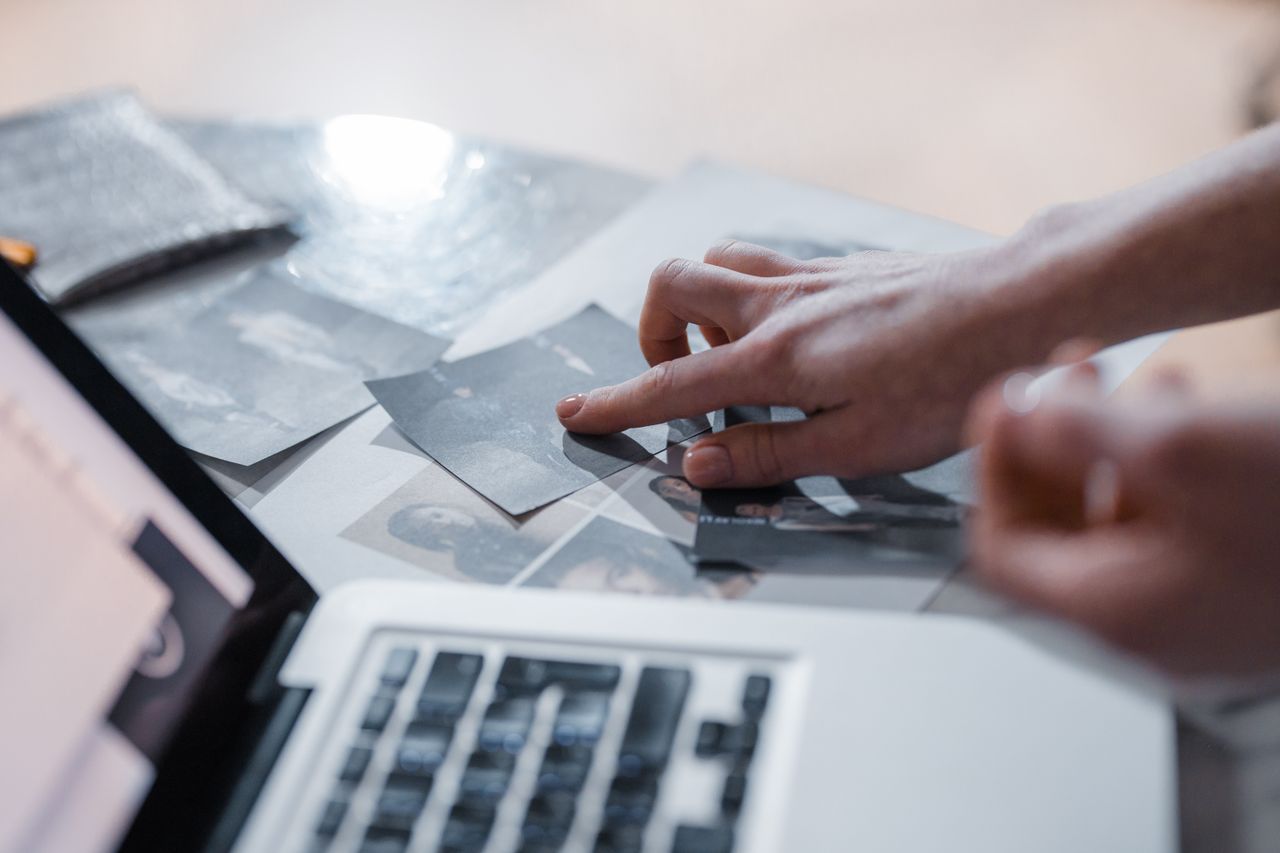 A hand arranges vintage photographs near a laptop in a modern workspace.