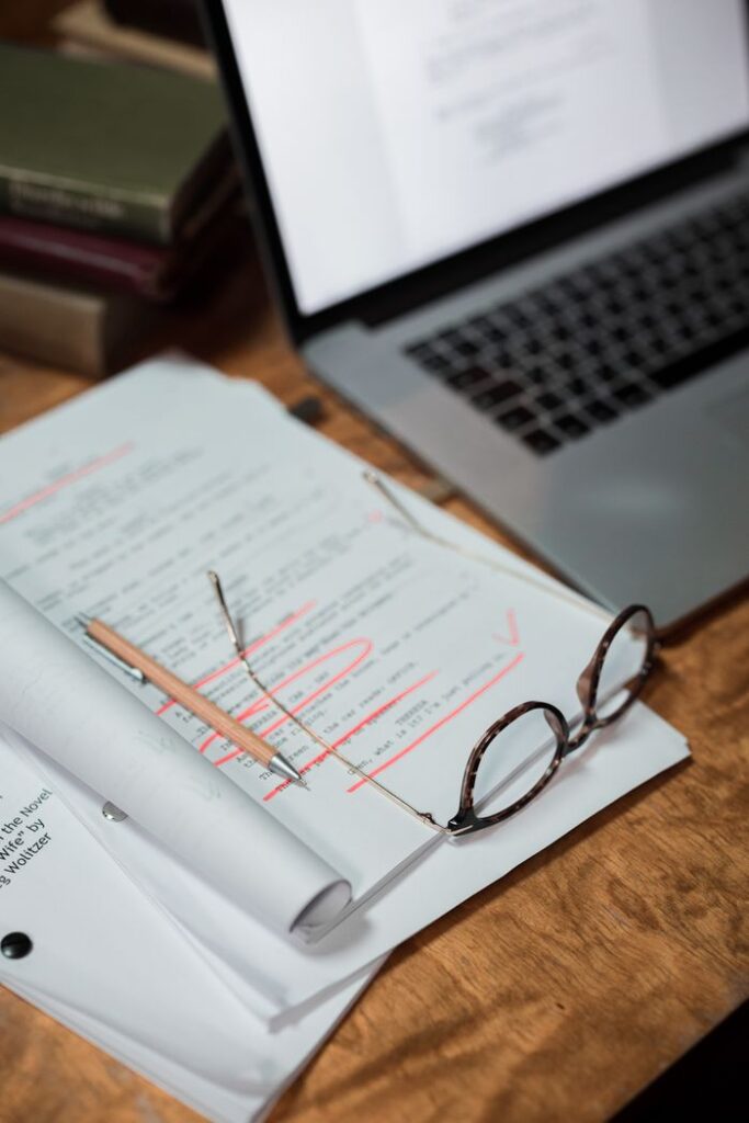 Glasses and documents on a desk with a laptop, representing a busy workspace.